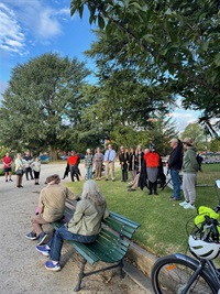 People standing around and seated under large trees watching two performers in orange, grey and black coloured flying-fox costumes
